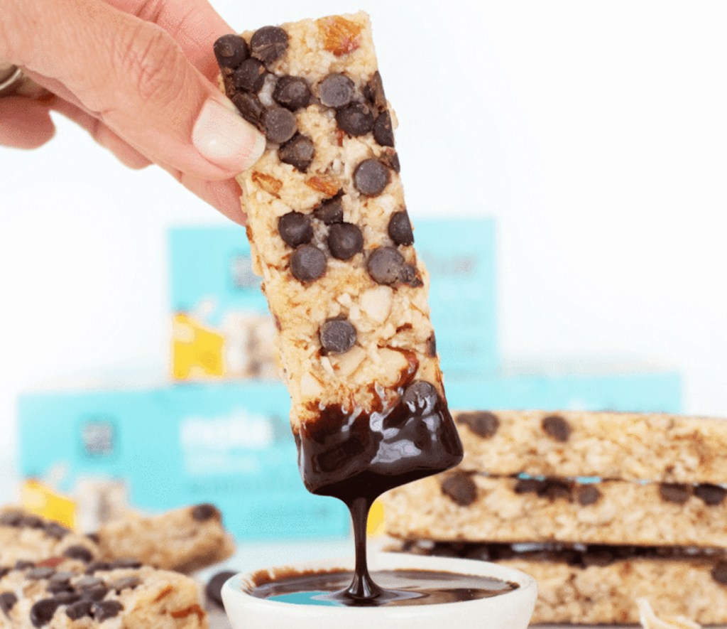 hand holding chocolate chip snack bar dipped in chocolate dripping into bowl