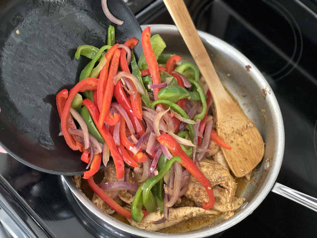 putting peppers and onions into skillet with chicken 