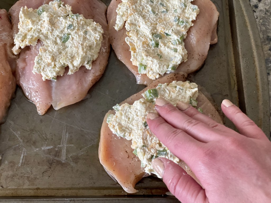 adding cream cheese mixture to chicken breasts for keto cream cheese stuffed chicken breasts