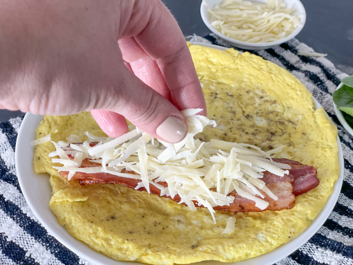 adding parmesan to a plate with bacon and eggs 