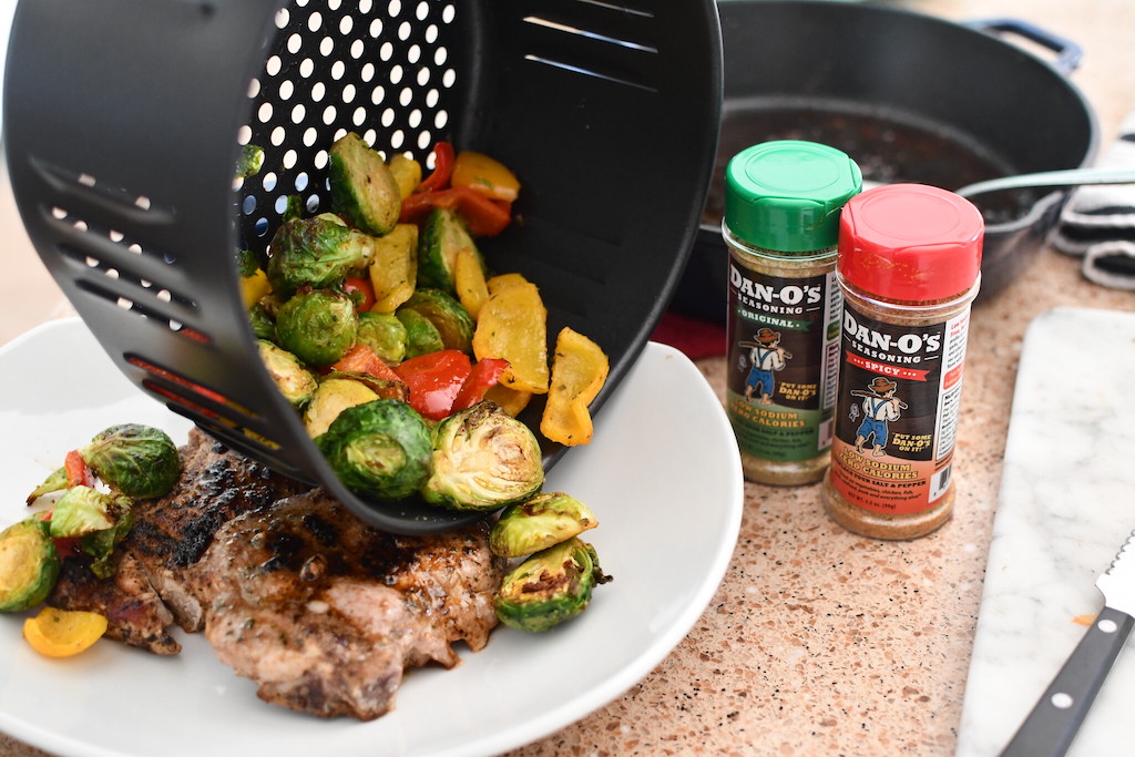 pouring air fryer veggies onto plate with pork chop 