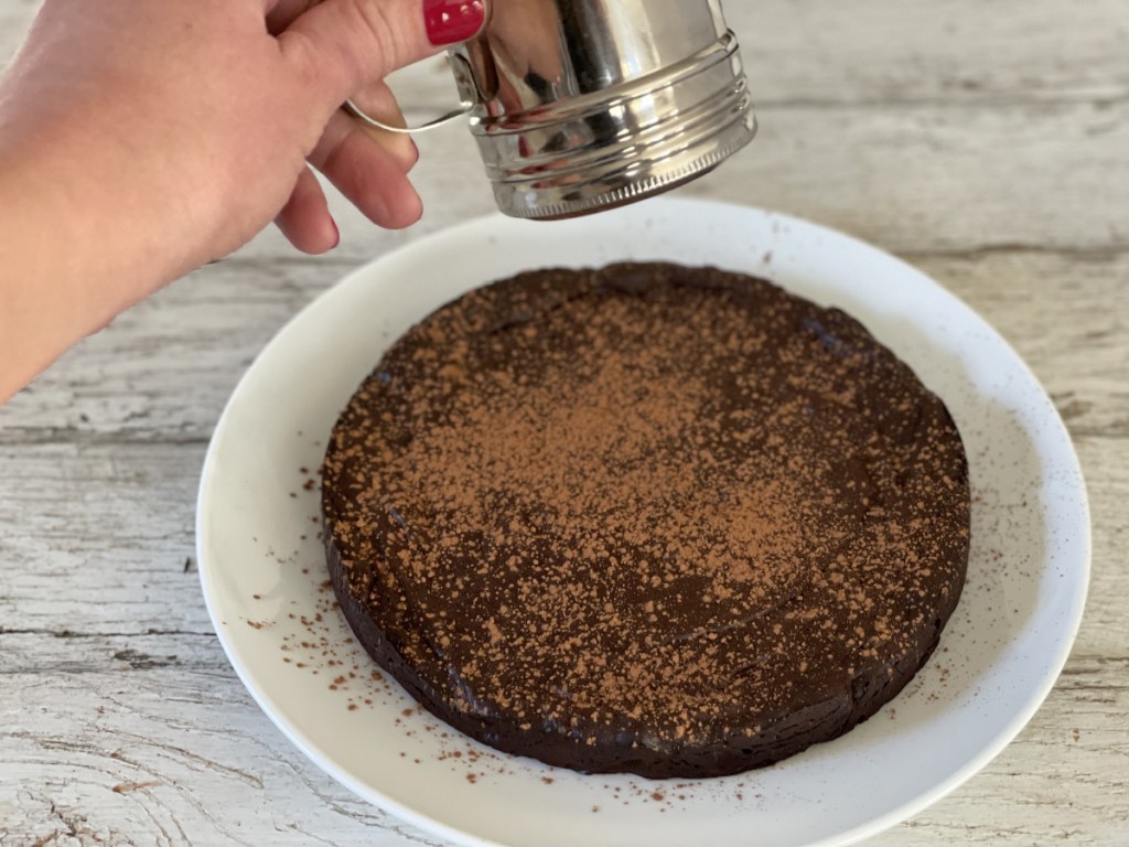 dusting keto flourless chocolate cake with cocoa powder 