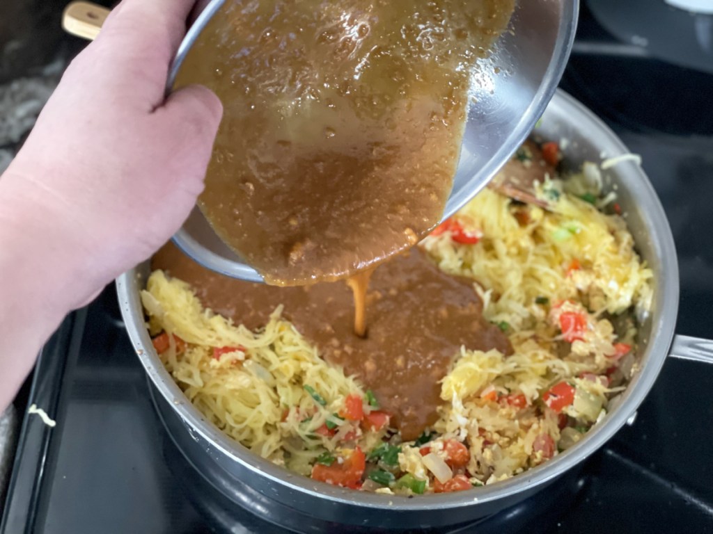 adding pad thai sauce to a skillet with vegetables 