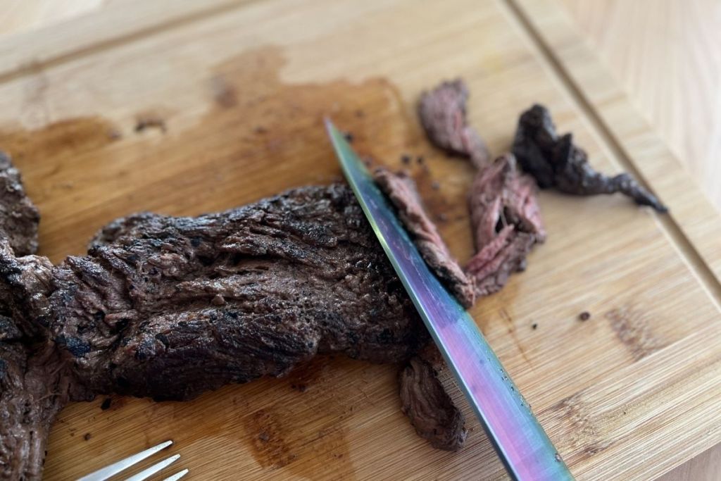slicing a piece of cooked carne asada