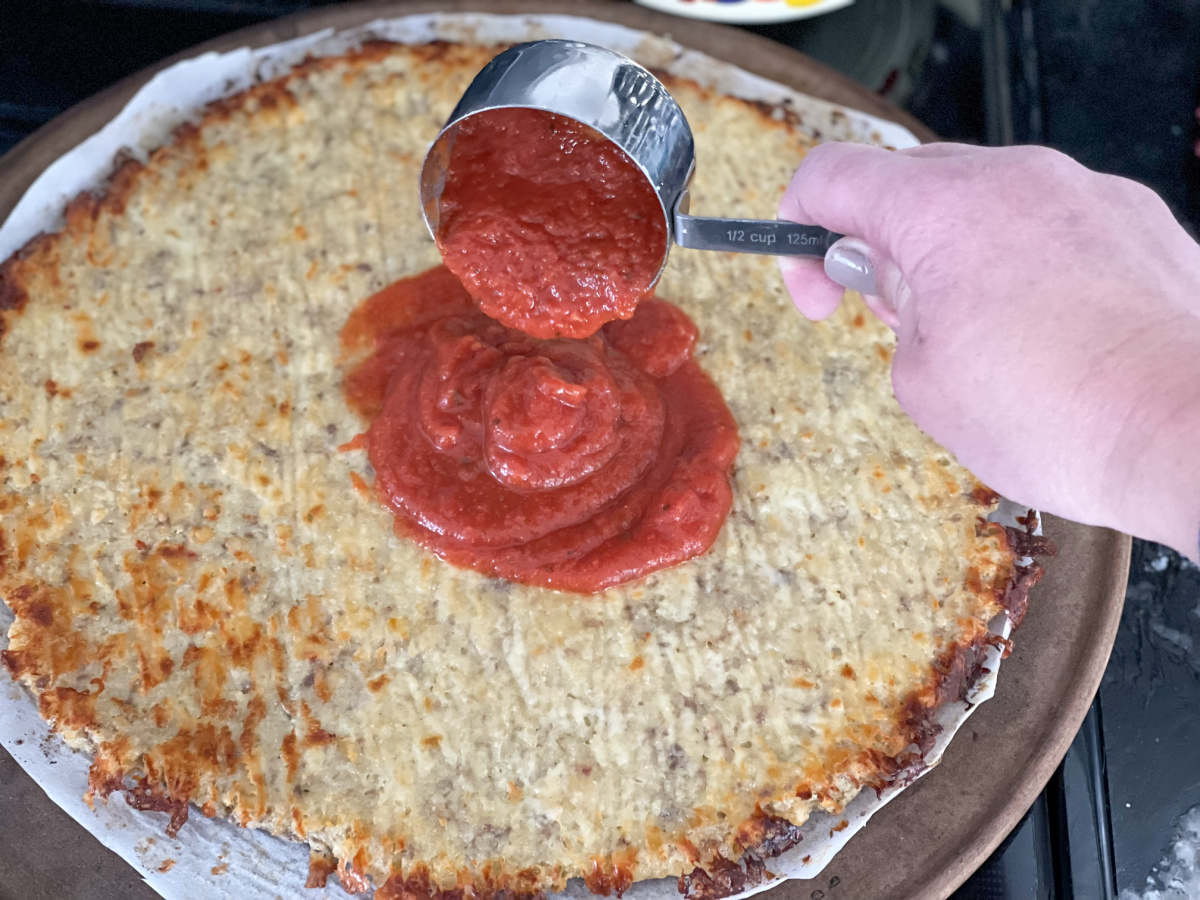 adding sauce to pizza crust