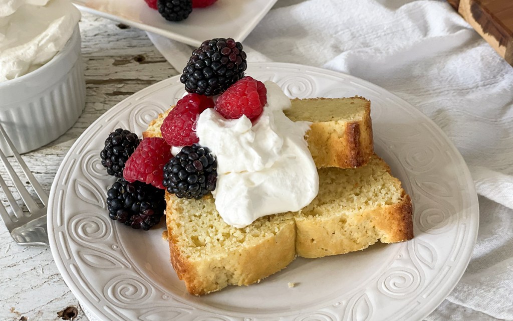 keto pound cake on plate with whipped cream and berries