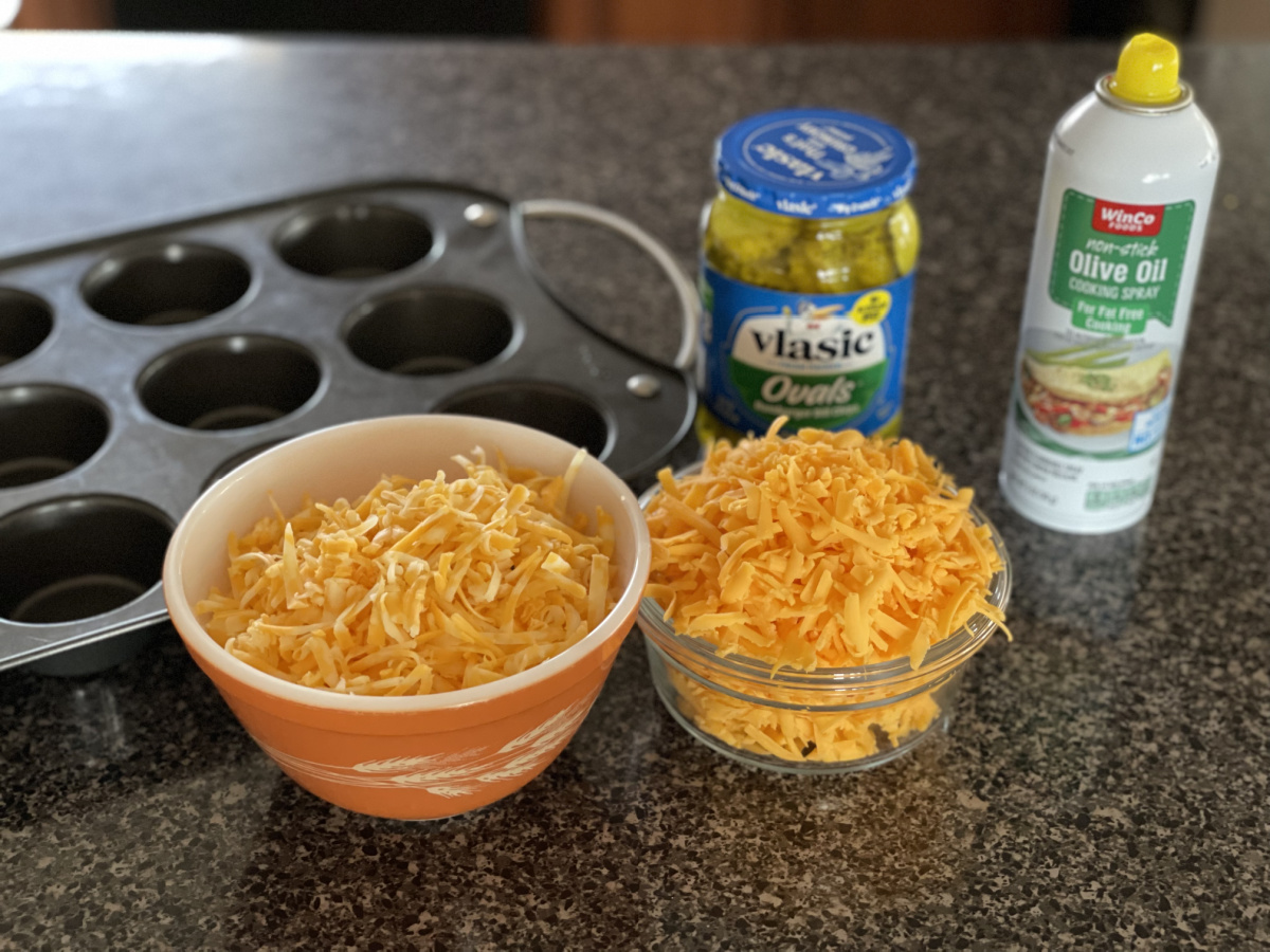 two bowls of cheese, pickles, olive oil spray, and a muffin tin