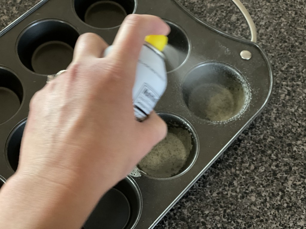 spraying muffin tin with nonstick spray
