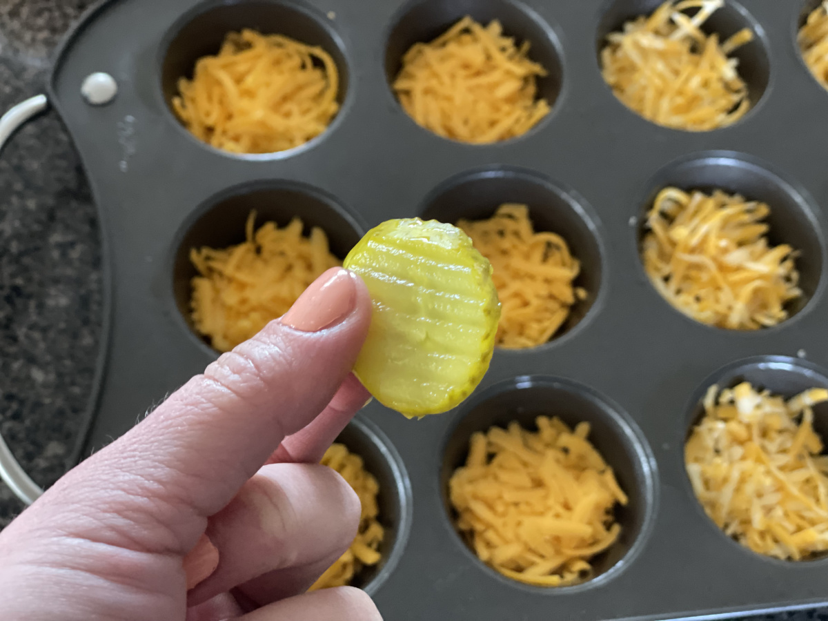 hand holding a pickle slice above muffin tin