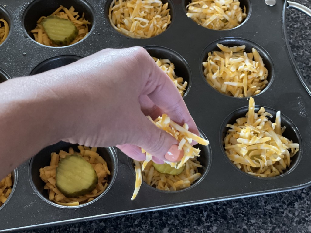 putting cheese on top of pickles in muffin tin