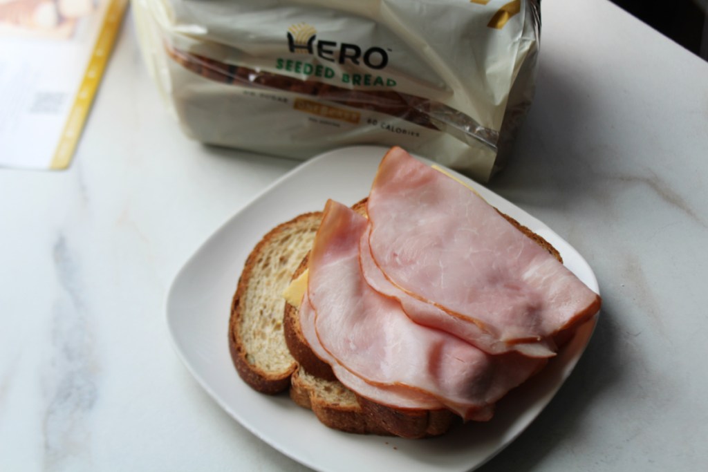 A loaf of Hero Seeded Bread next to a ham sandwich on a plate
