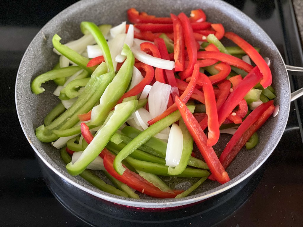sliced bell peppers and onions in a skillet 