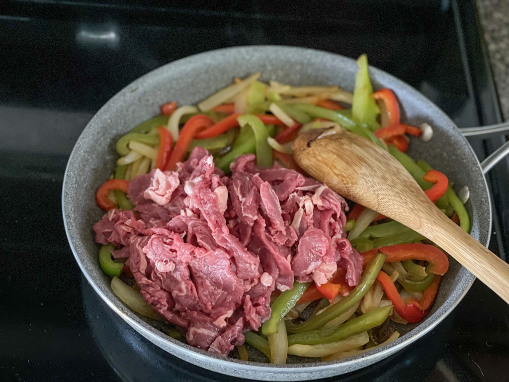 sliced steak in a skillet with peppers and onions