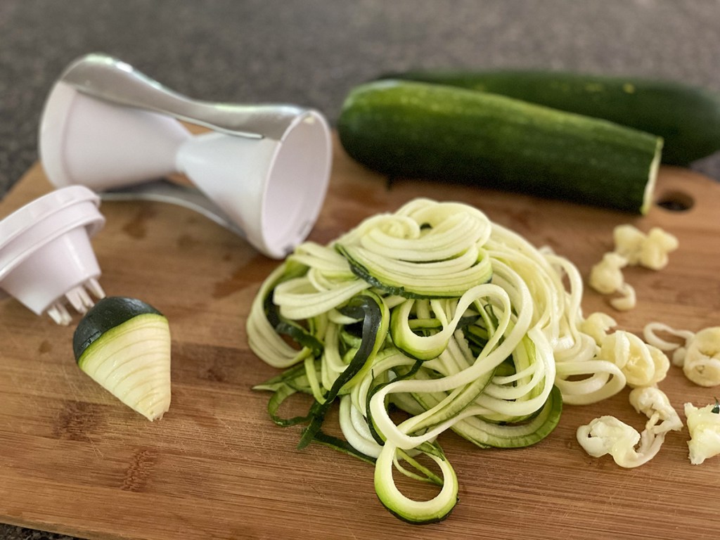 zoodles on cutting board with handheld spiralizer