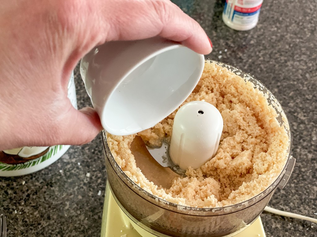adding melted coconut oil to puréed coconut in food processor 