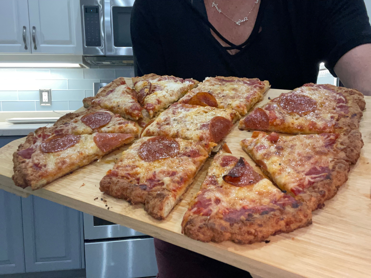 holdling keto sausage crust pizza on a cutting board