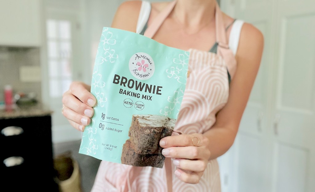 woman holding keto brownie mix packet standing in kitchen with apron