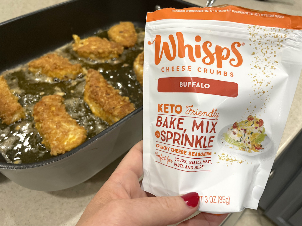 holding bag of Whisps cheese crumbs with chicken in pan