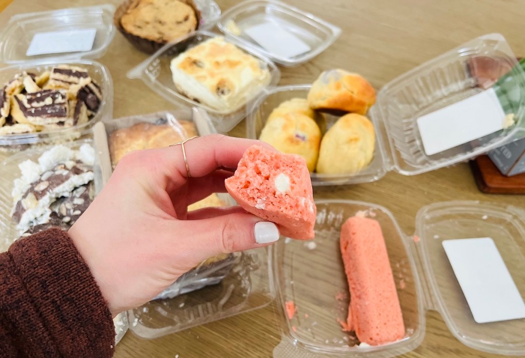 hand holding pink twinkie over takeout containers of keto bakery treats