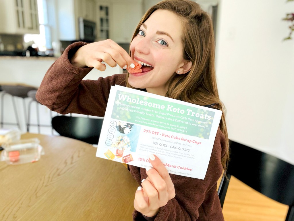 woman holding wholesome keto treats flyer in hand while eating pink twinkie