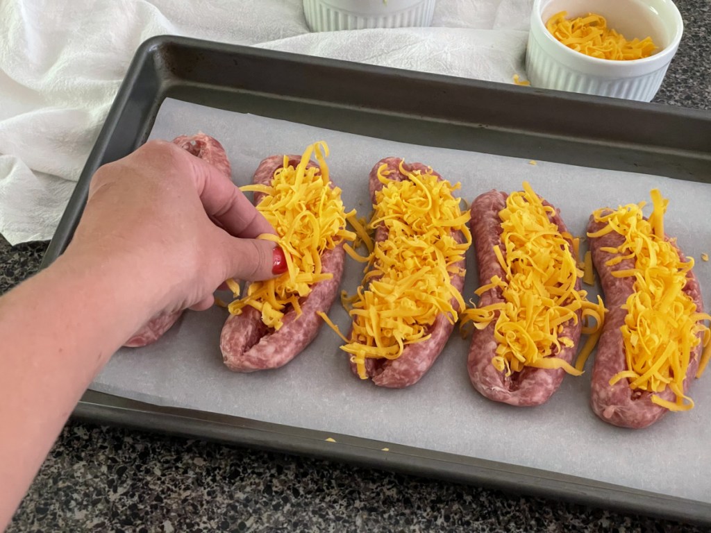 adding shredded cheese to sliced open sausages