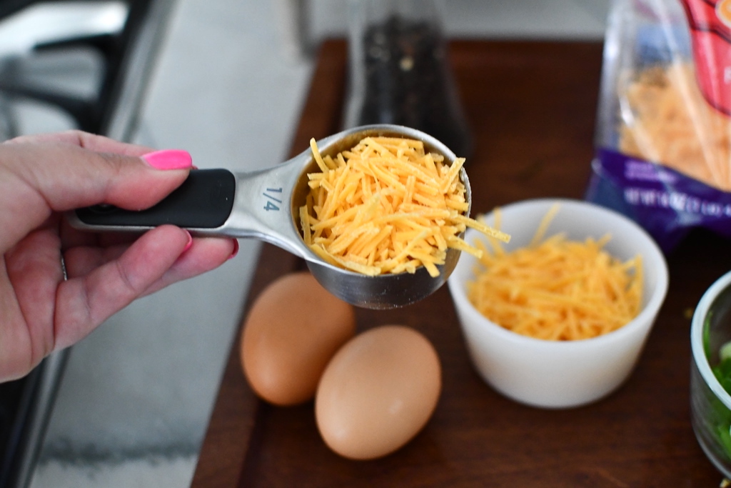 shredded cheese in measuring cup with eggs in background