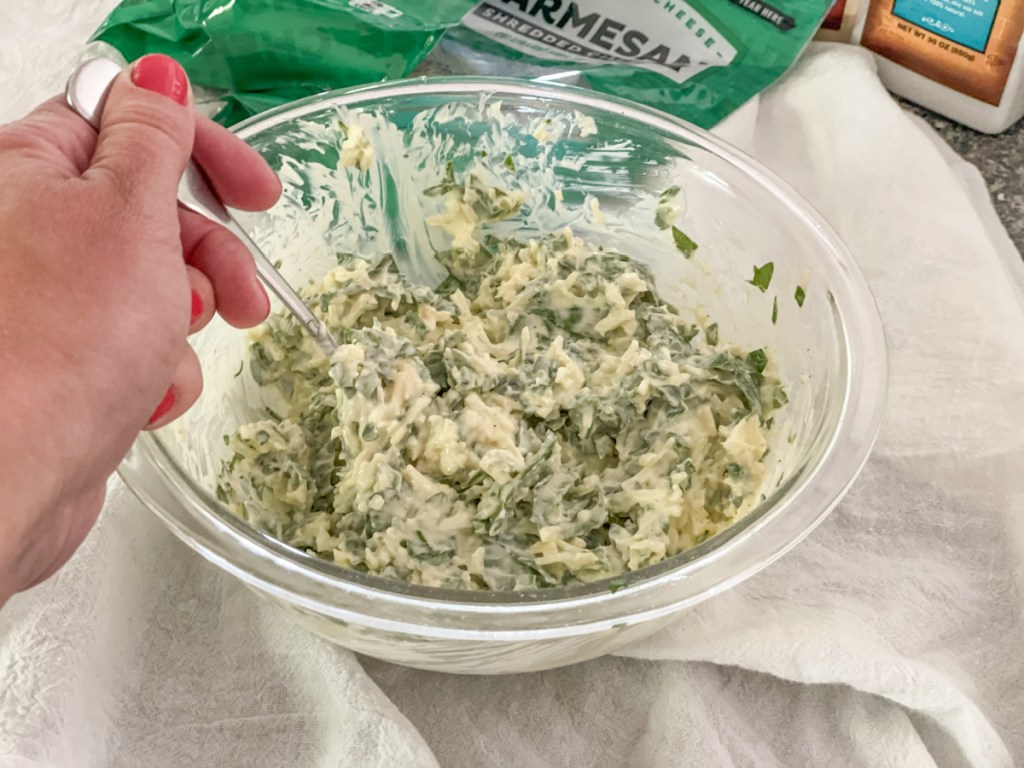 mixing together mayonnaise, shredded cheese, seasonings, and spinach
