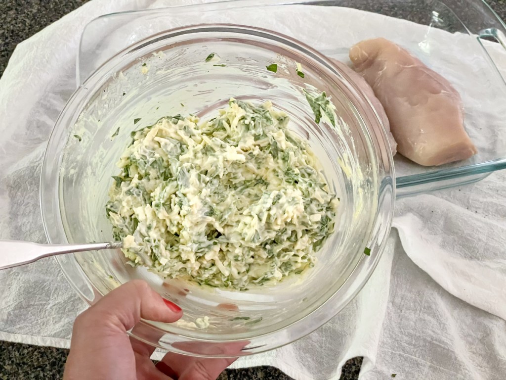 bowl of mixed together mayonnaise, shredded cheese, chopped spinach, and seasonings