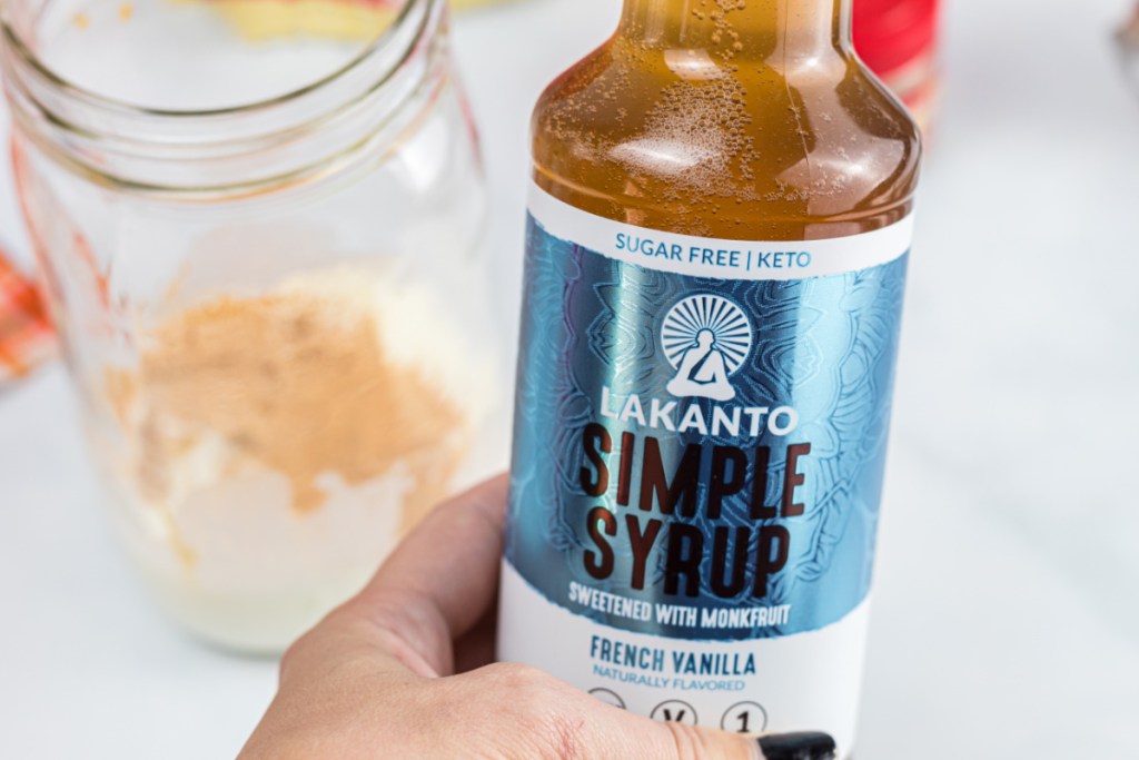 Hand holding lakanto simple syrup which will be used in a low carb pumpkin cream cold brew