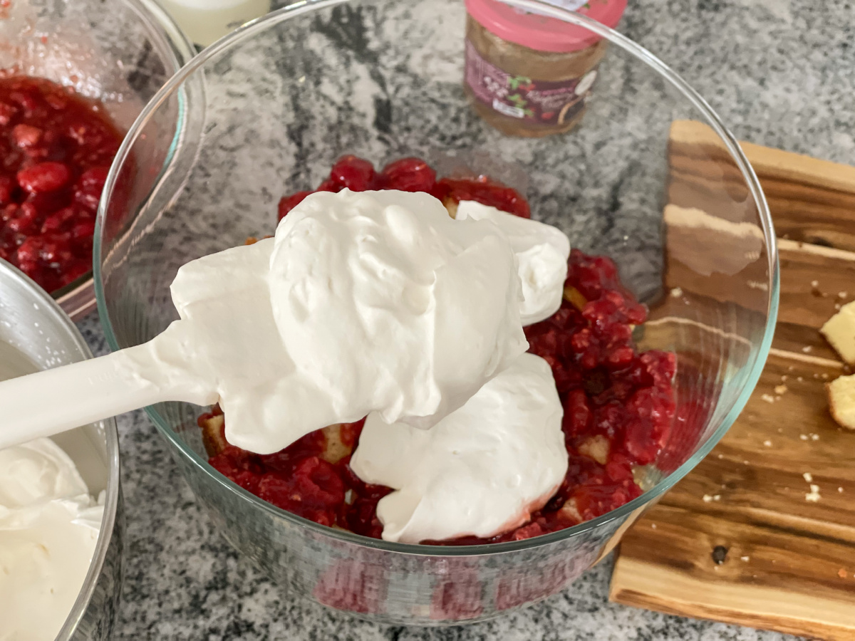 adding whipped cream to trifle bowl