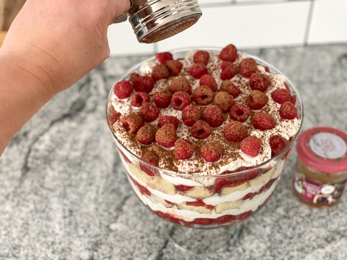 sprinkling cocoa powder over keto raspberry trifle