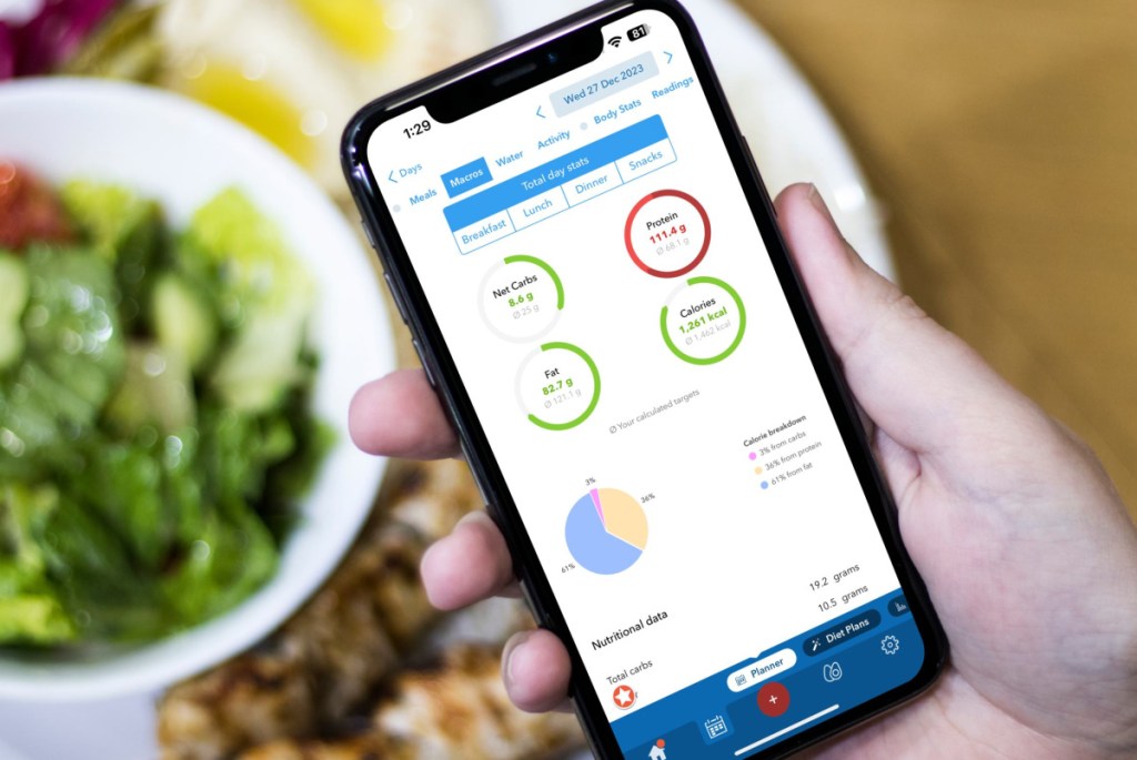 table with food and hand holding an iphone showing KetoDiet, one of the best keto apps of 2024