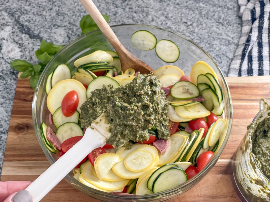 adding pesto to zucchini salad