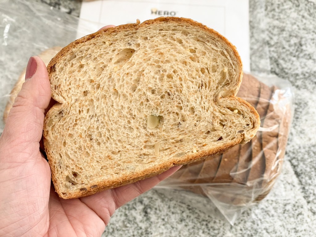 holding slice of Hero Bread seeded bread