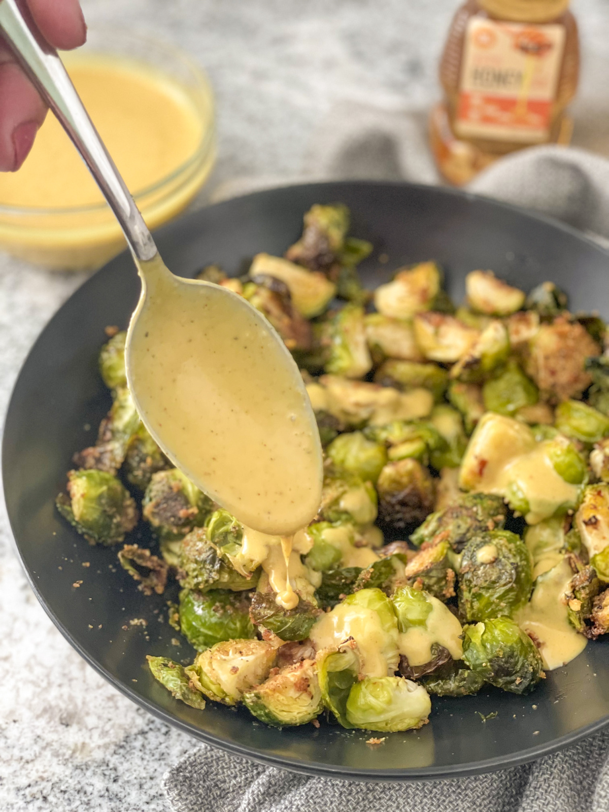 drizzling keto honey mustard sauce over Brussels sprouts