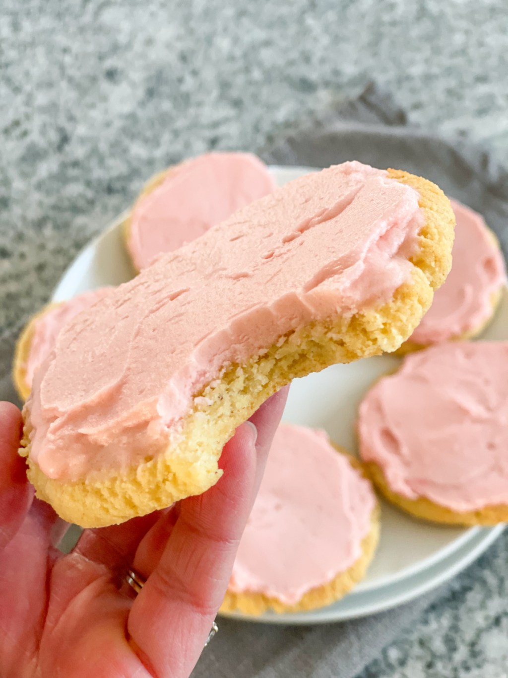 holding a keto crumbl pink sugar cookie with a bite out of it