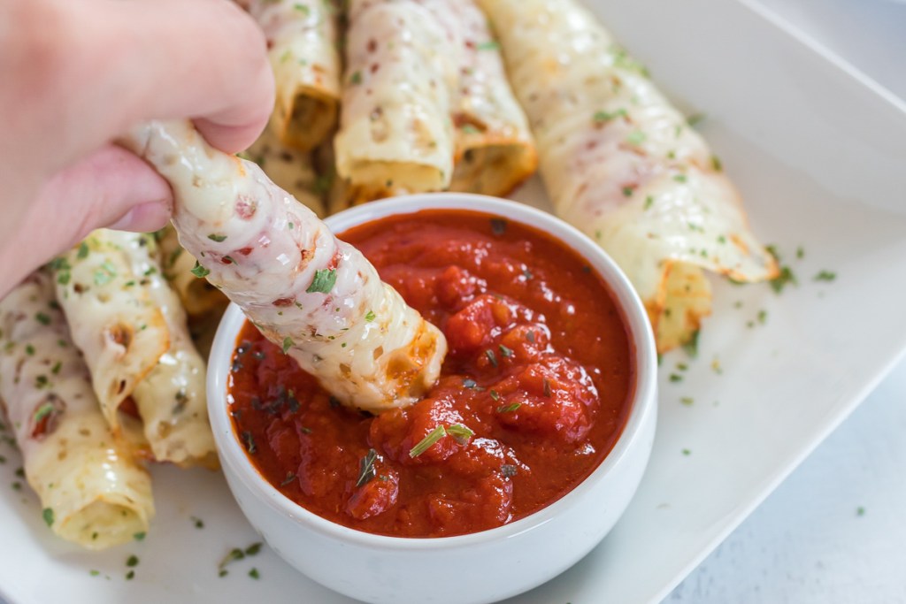 Dipping pizza roll ups in marinara sauce as high protein low carb snacks
