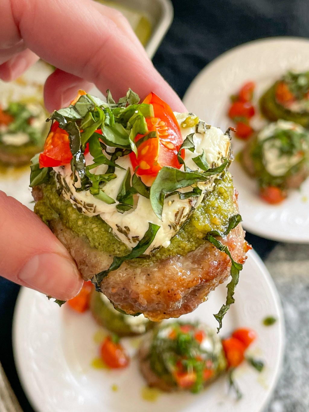 holding sausage bites with pesto, goat cheese, tomatoes