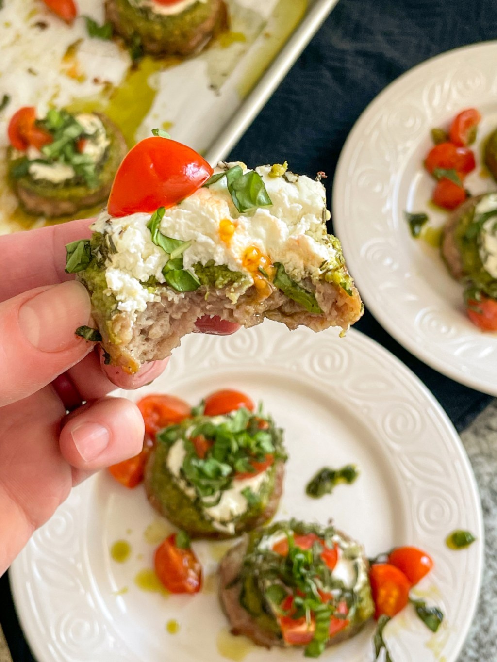 holding sausage bites with pesto, goat cheese, tomatoes with a bite out of it