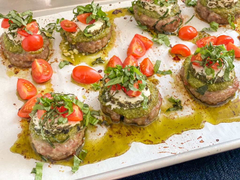 sausage bites with pesto, goat cheese, tomatoes on baking sheet 