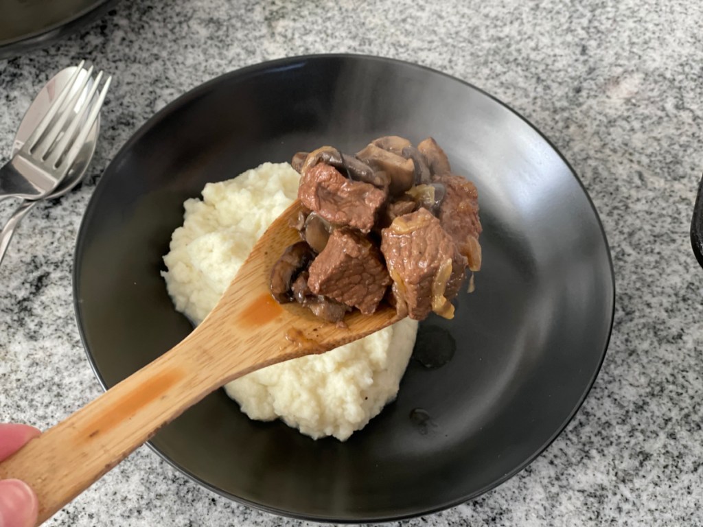 serving beef tips onto a plate with mashed cauliflower