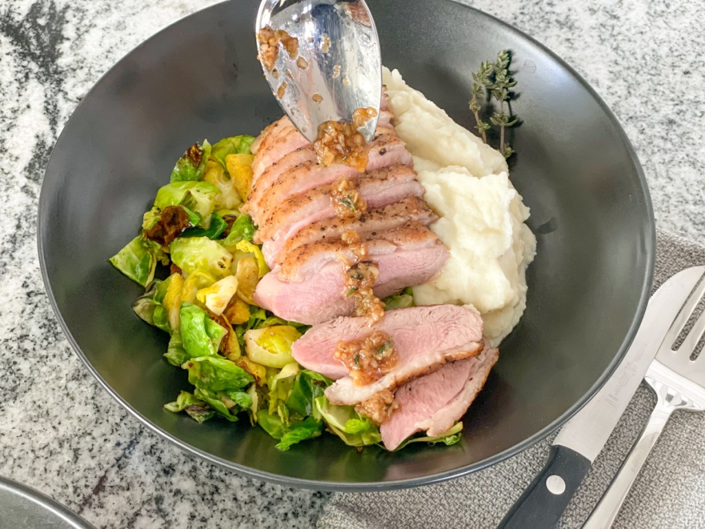 adding garlic sauce to plated duck breast with mashed cauliflower and Brussels sprouts