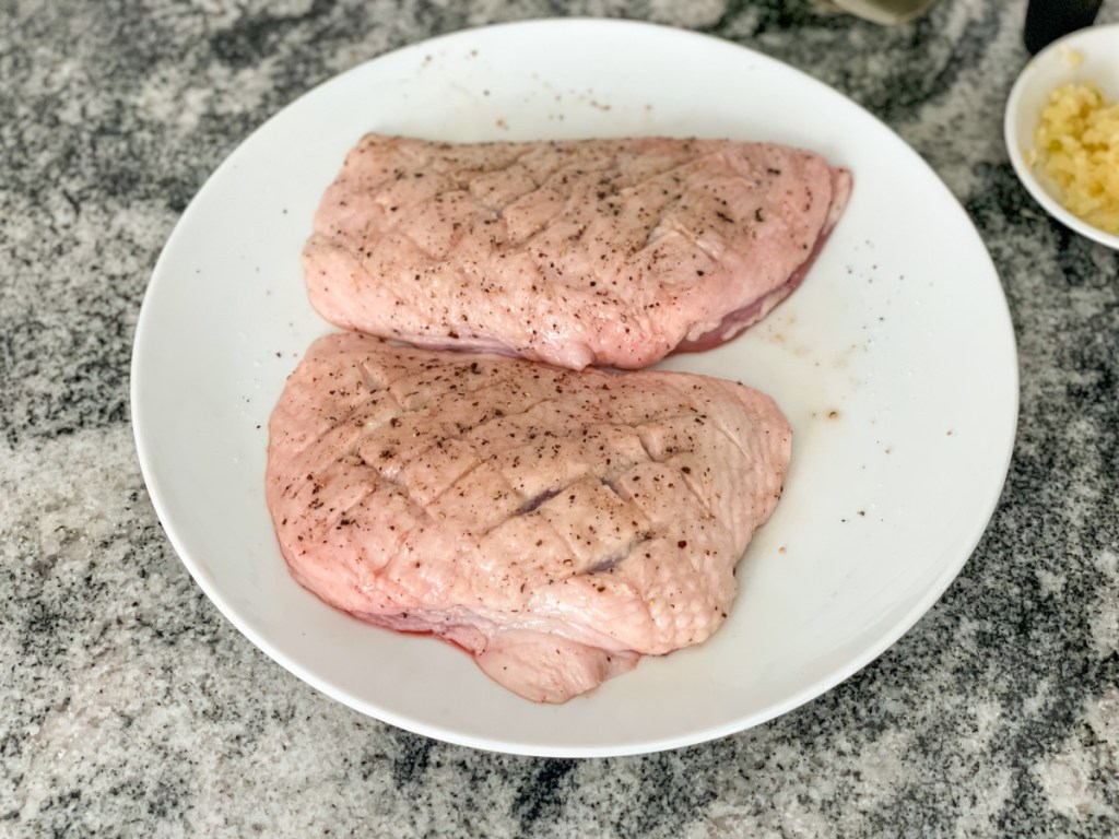 raw duck breasts with skin scored on a plate