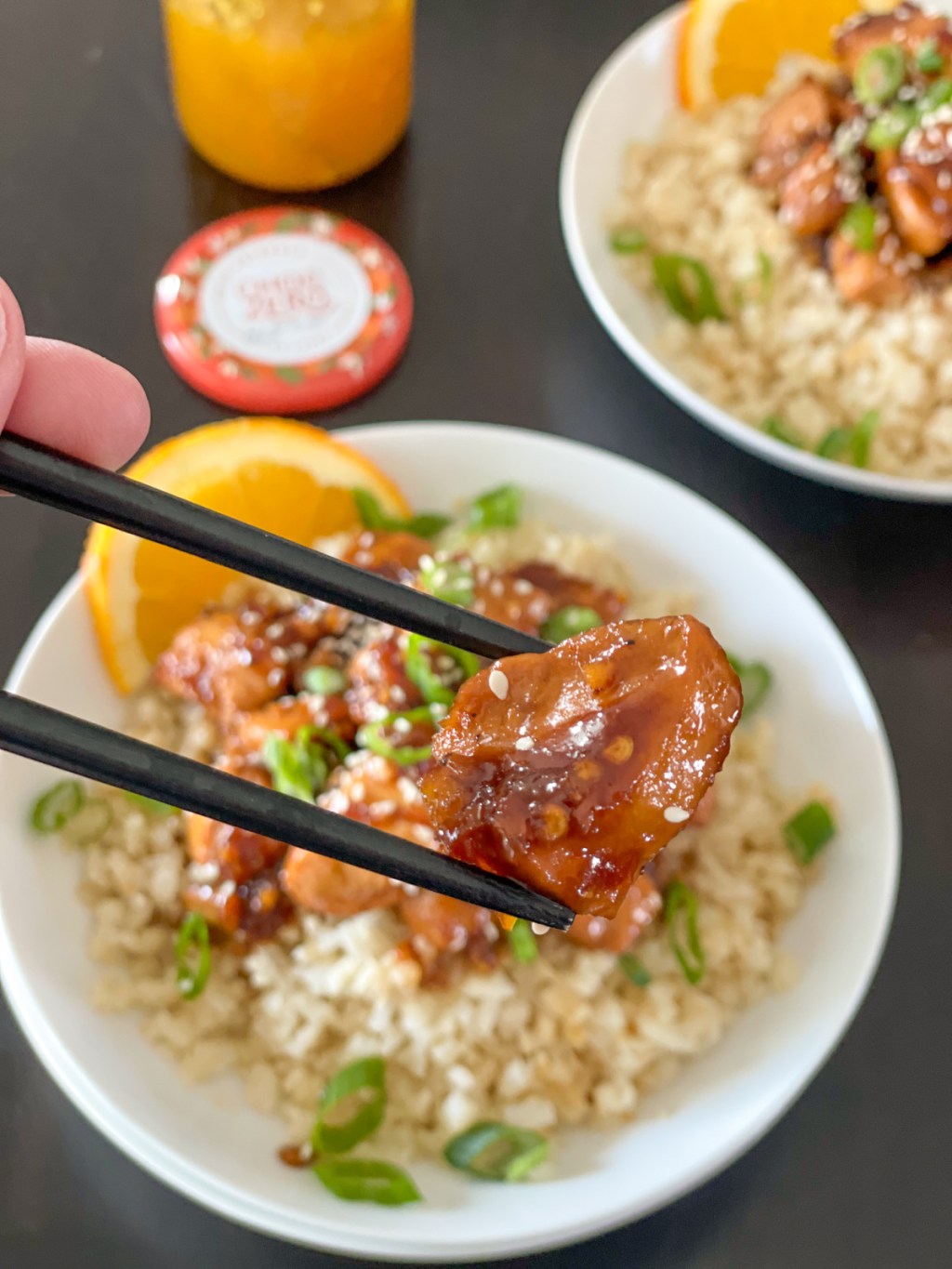 holding a piece of orange chicken with chopsticks