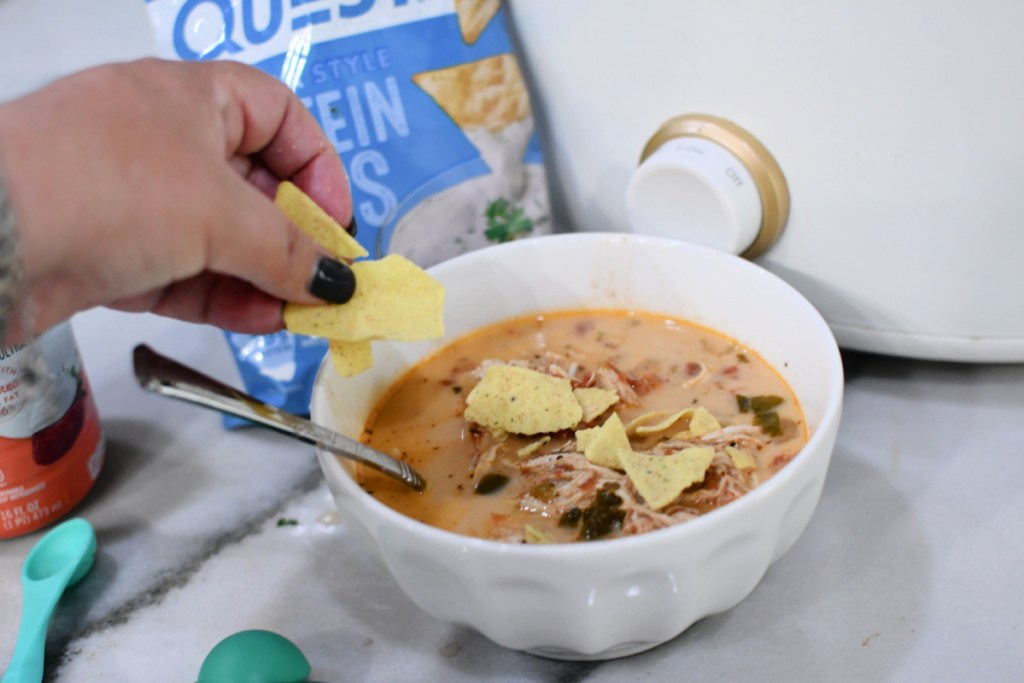 Topping a bowl of keto soup with Quest chips.