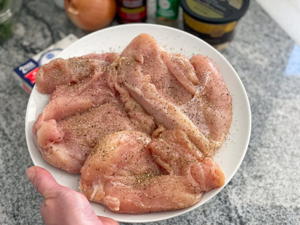 holding a plate of seasoned chicken breasts 