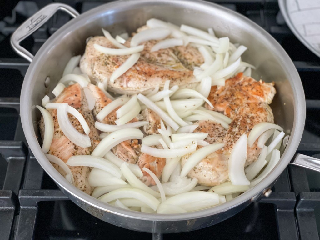 seared chicken breasts in a skillet with sliced onion