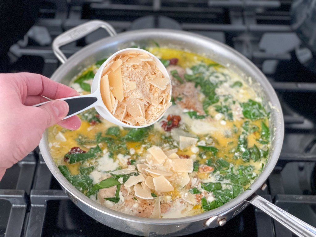 adding shaved parmesan to a skillet with chicken and cream sauce 