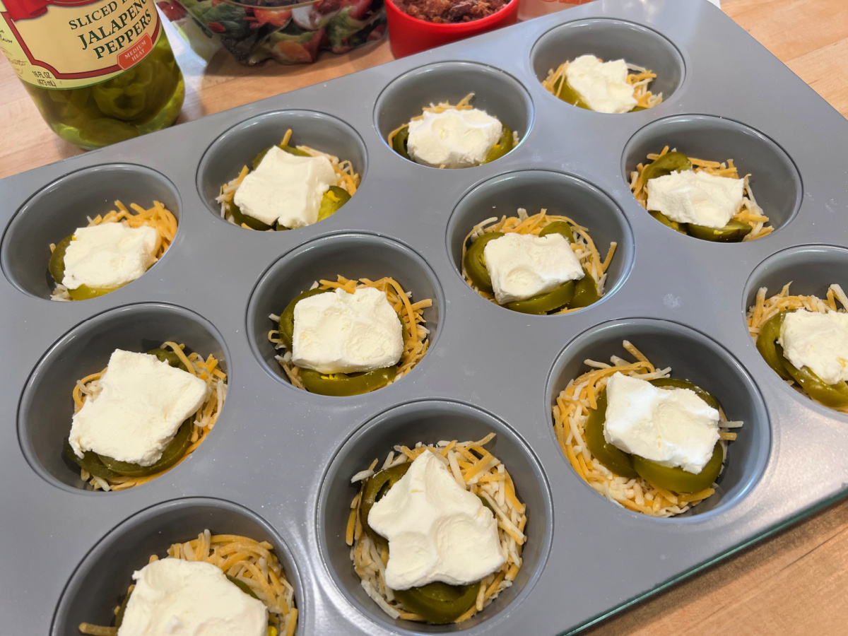 Muffin tine prepped with shredded cheese, jalapeños and cream cheese cubes.