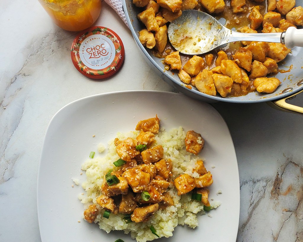 plate of keto orange chicken next to skillet and choczero orange marmalade jar